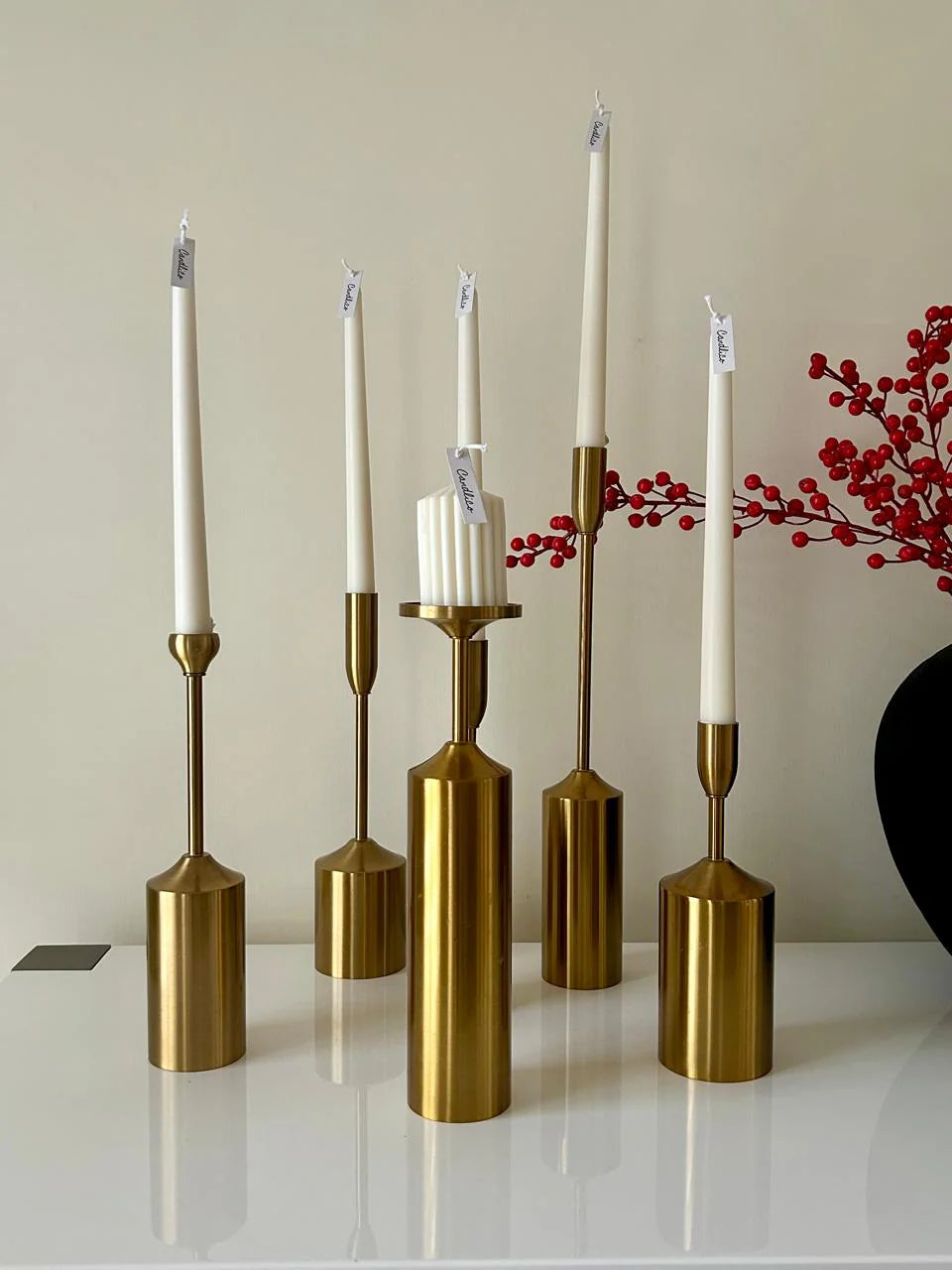 Set of gold candle holders with candles on a reflective surface